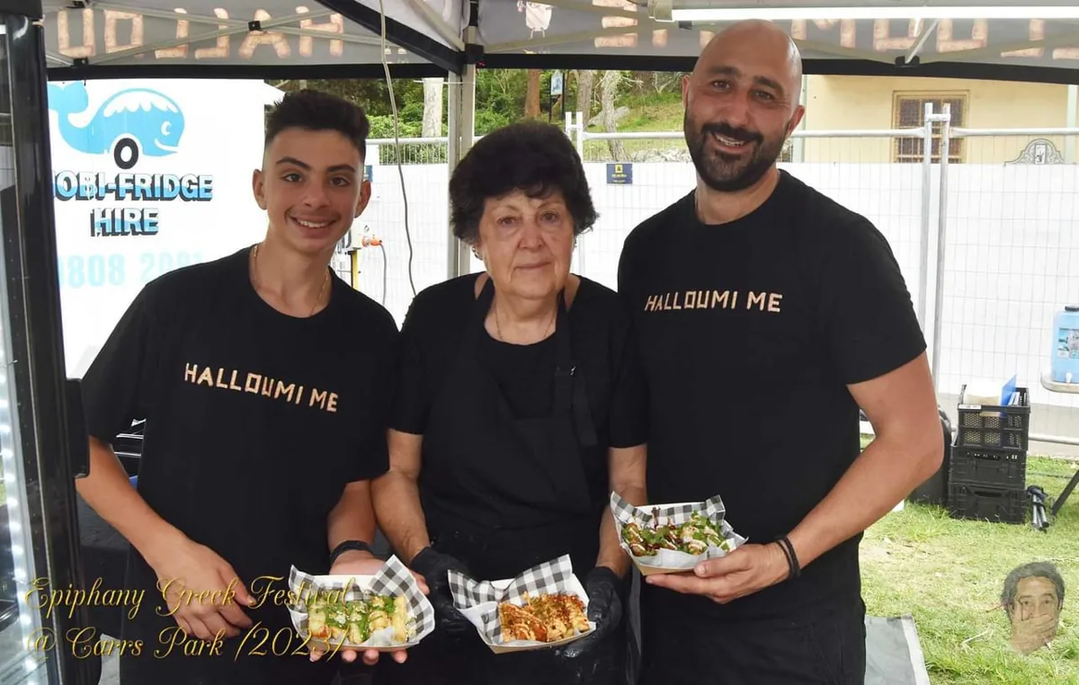 The Halloumi Me team in black branded T-shirts, holding trays of food at the Epiphany Greek Festival